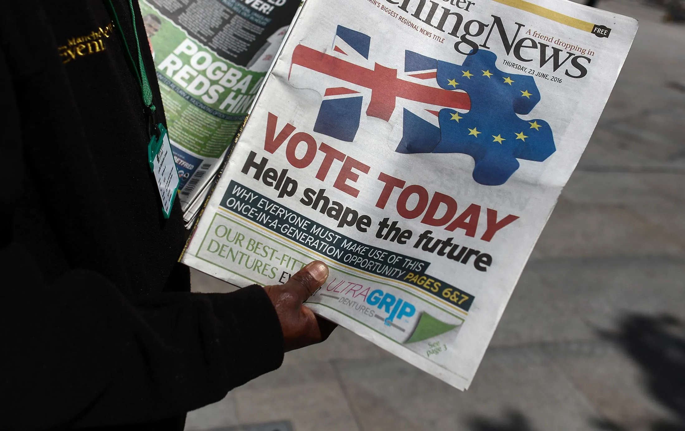 A vendor holds out copies of the Manchester Evening News newspaper at the Town Hall in Manchester, U.K.

