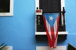 A for sale sign is seen hanging from a balcony next to a Puerto Rican flag in Old San Juan.
