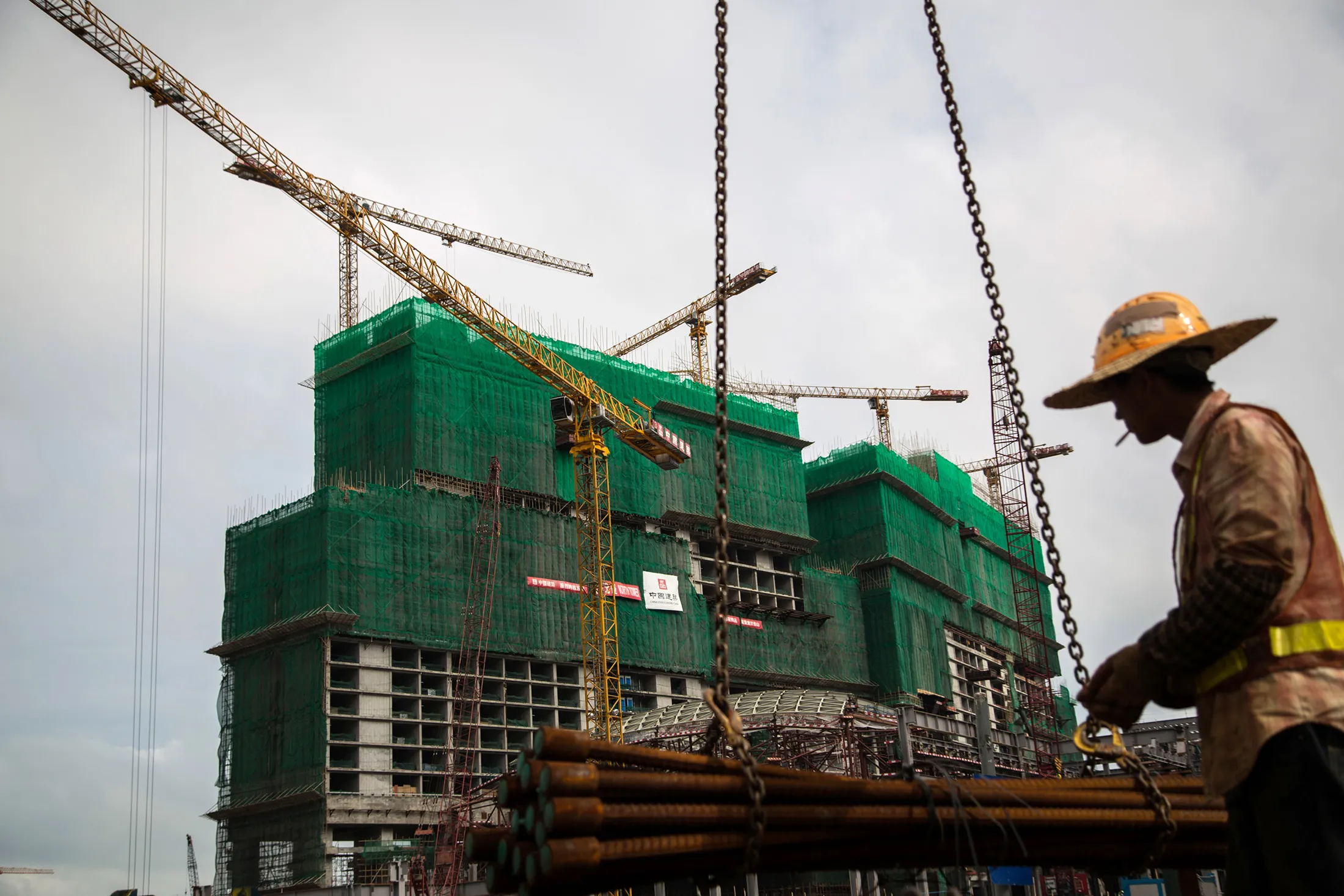 A worker smokes a cigarette as cranes operate at the construction in Macau, China, on May 10, 2015.
