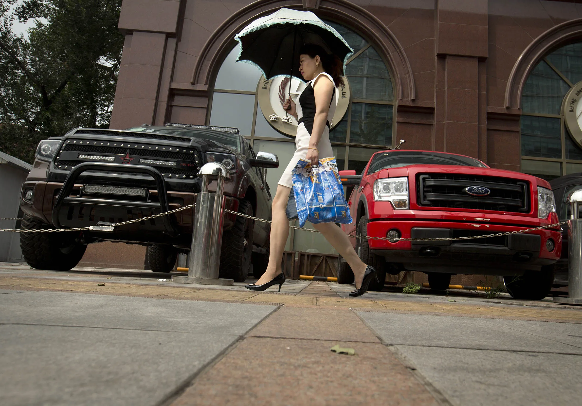 A woman walks past pickup trucks parked outside a luxury import car dealership in Beijing. Pickup trucks are being allowed in select urban areas for the first time as the government seeks to revitalize the auto industry.
