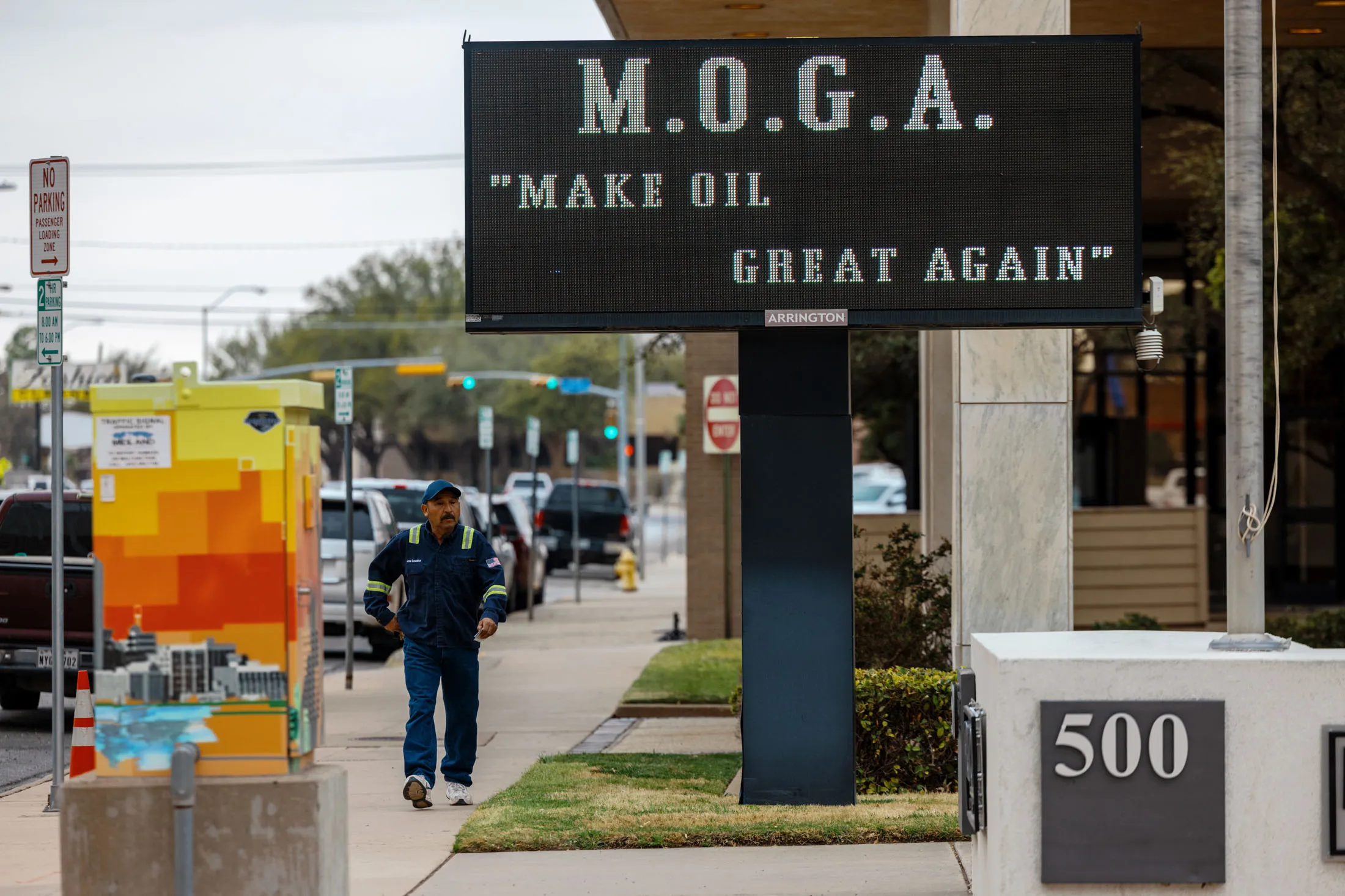 An oilfield worker walks past a sign that reads "M.O.G.A 'Make Oil Great Again'" in downtown Midland.