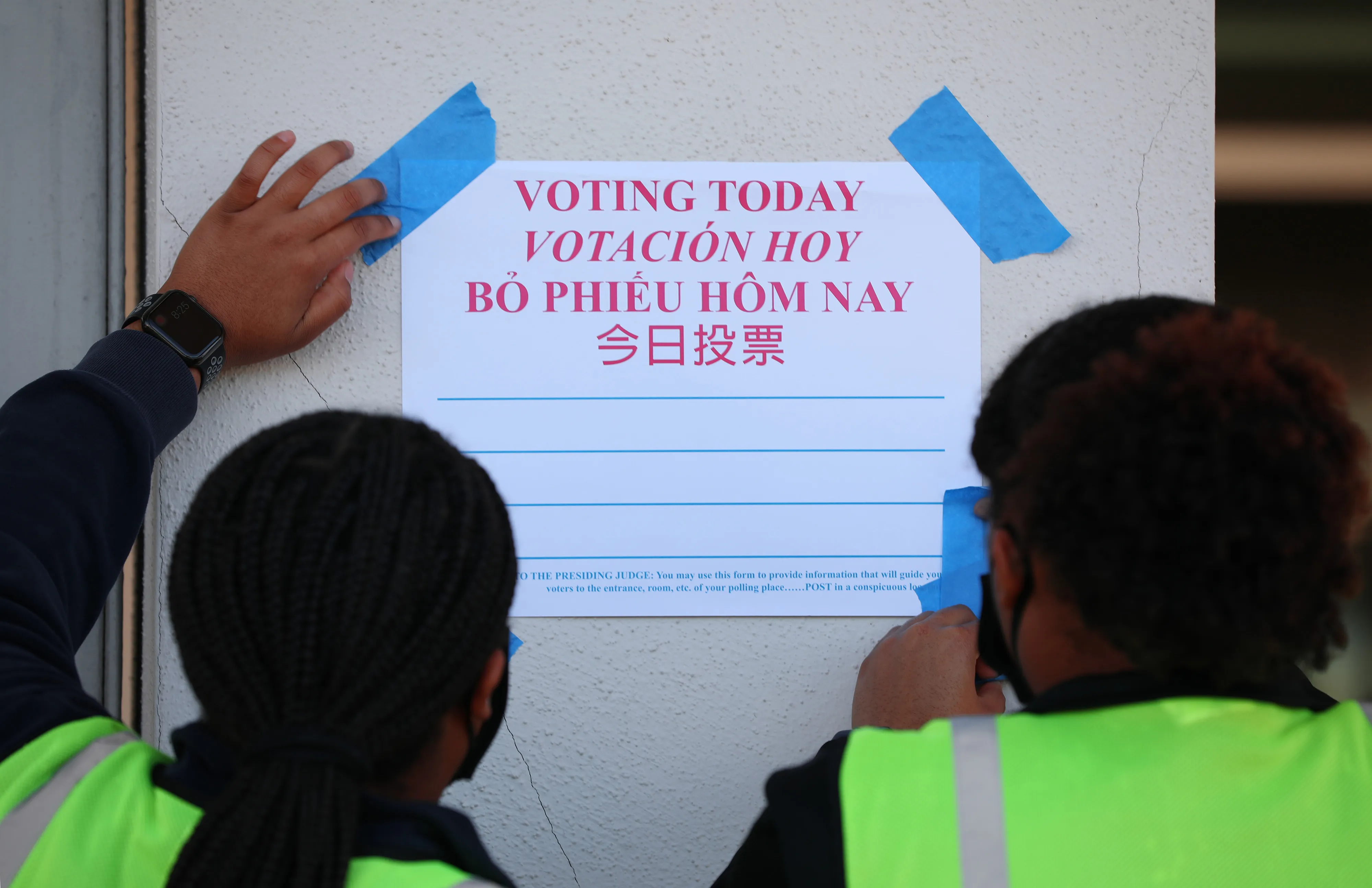 Election officials tape a "Voting Today" sign outside a polling location for the 2020 Presidential election.