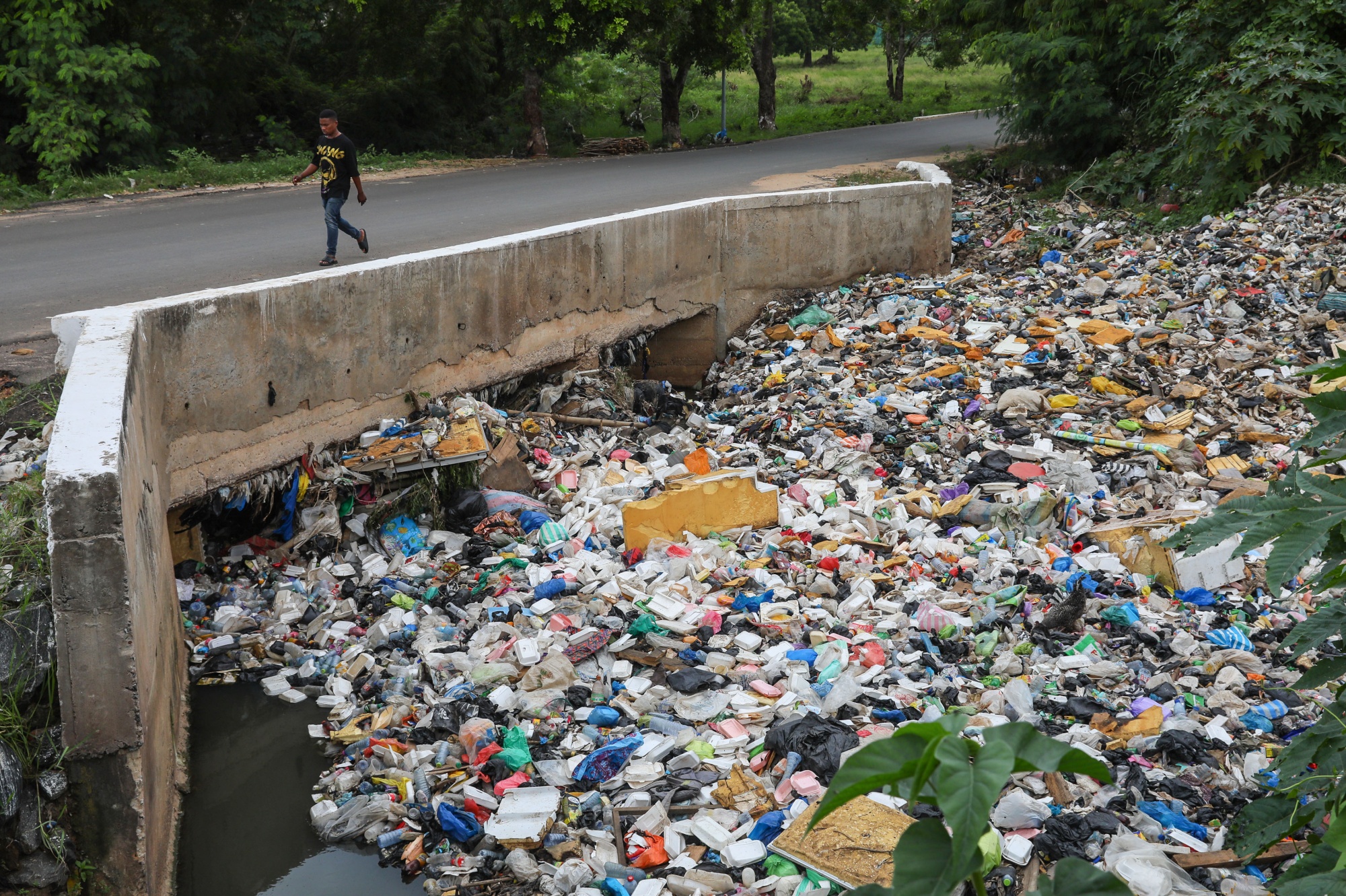 A pedestrian walks along a bridge over a gutter, blocked by plastic waste and garbage, in Accra, Ghana.