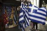 A woman unfolds a souvenir Greek national flag hanging outside a street vendor's kiosk in Athens, Greece, on Tuesday, Feb. 28, 2017.&nbsp;