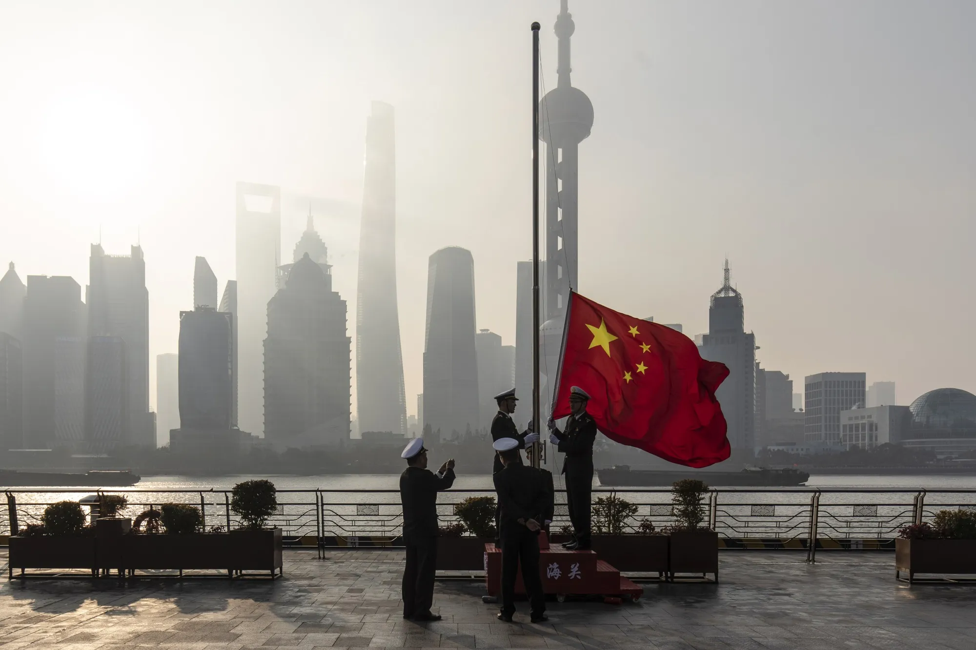 China Customs officers raise a Chinese flag along the Bund in front of the Lujiazui Financial District at sunrise in Shanghai, China.