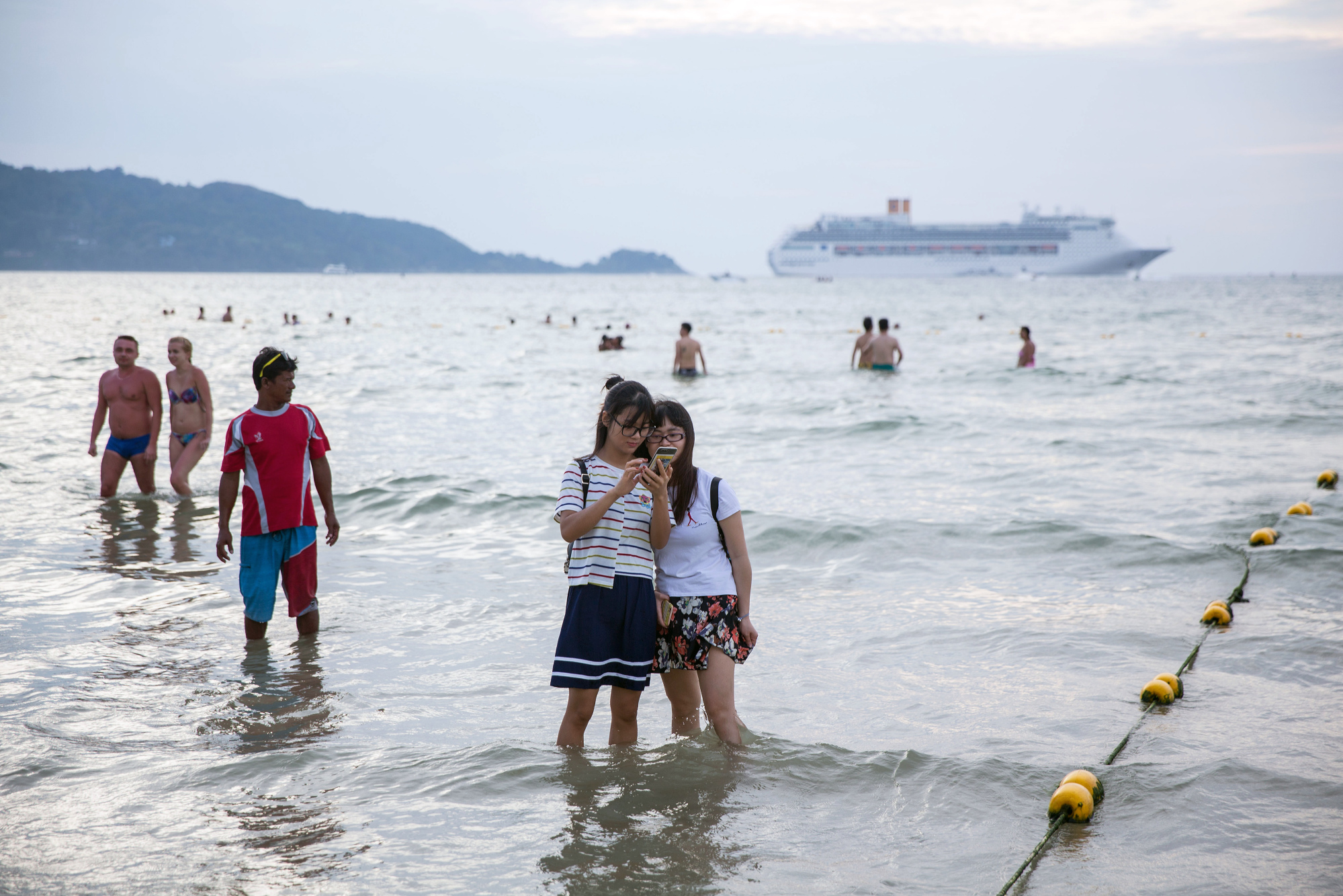 Tourists look at a selfie while standing in the sea at Patong Beach in Patong, Phuket, Thailand.