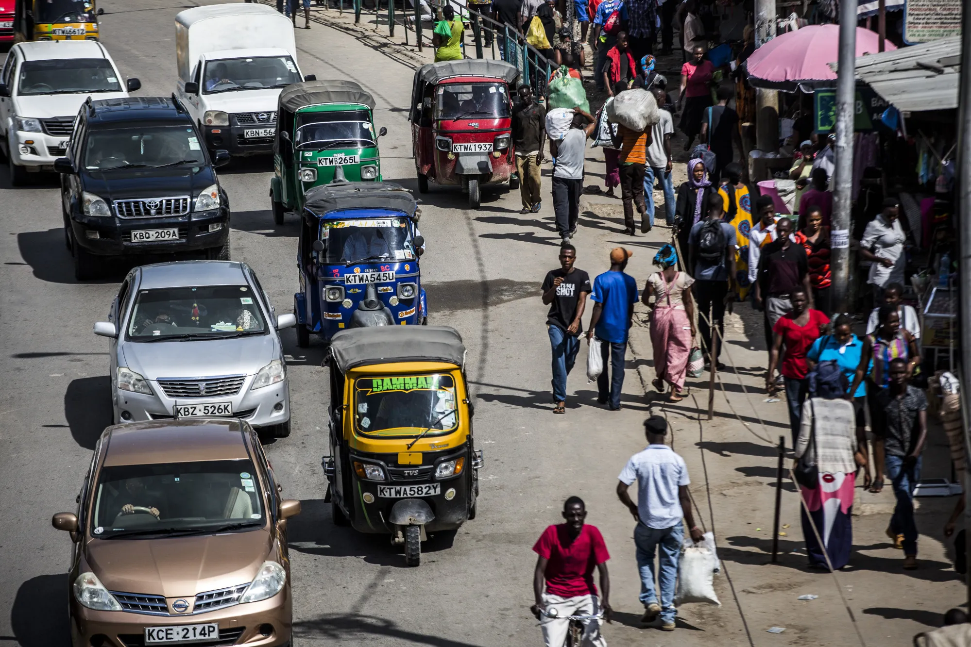 Automobiles and tuk-tuk drivers travel alongside pedestrians in Mombasa, Kenya.