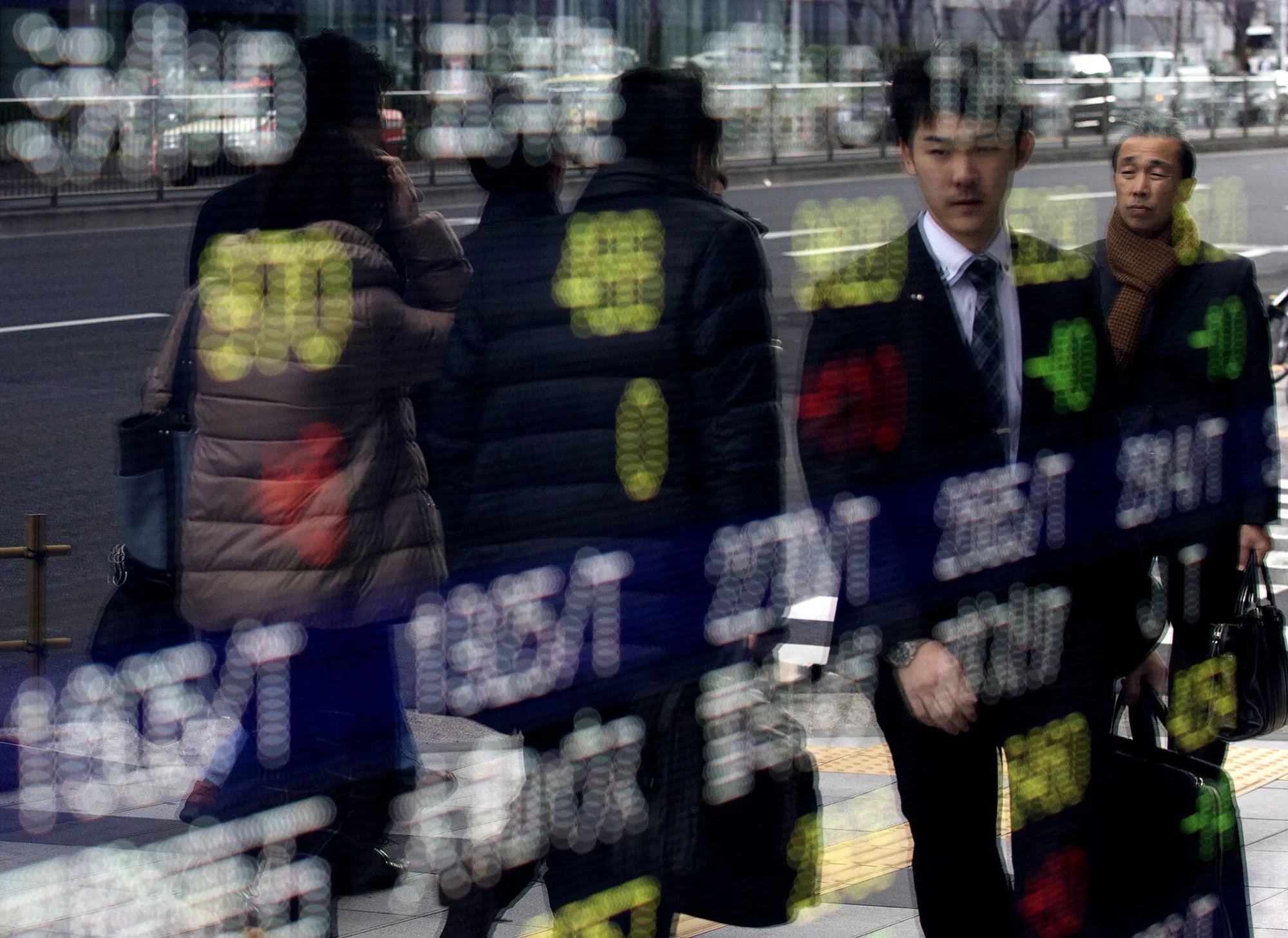 Pedestrians are reflected in an electronic stock board outside a securities firm in Tokyo, Japan, on Thursday, Jan. 7, 2016. Japanese stocks fell for a fourth day, extending a global slide that's seen shares post their worst start to a year since 2000, after China again cut the reference rate for the yuan and trading in the world's second-biggest equity market was halted.
