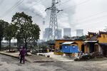 A woman walks past a temple as emission rise from cooling towers at a coal-fired power station in Tongling, China