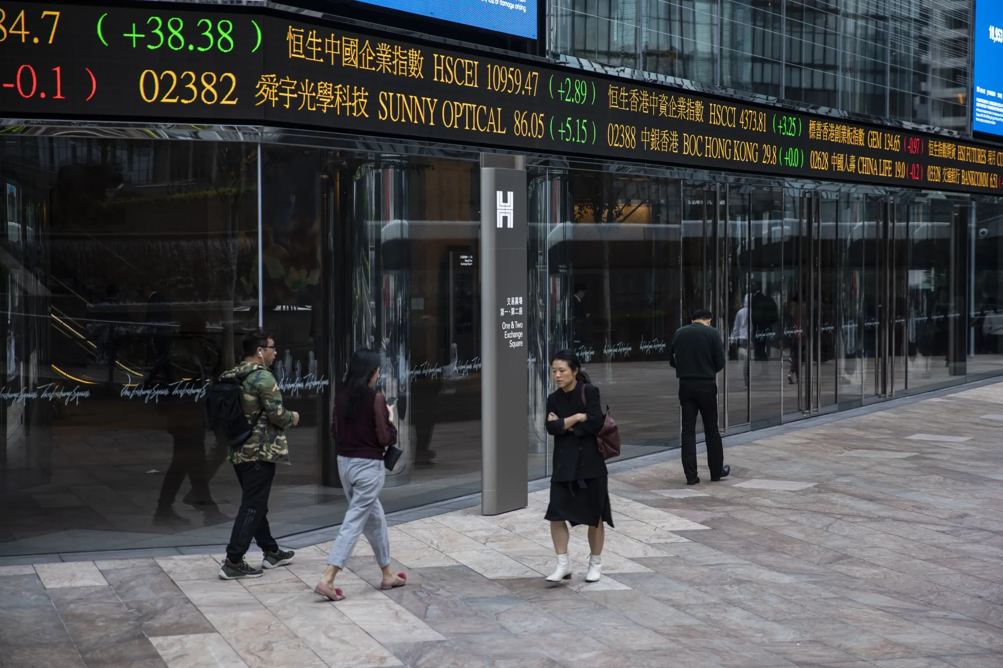 Pedestrians walk past an electronic ticker board&nbsp;outside&nbsp;the Hong Kong Stock Exchange.