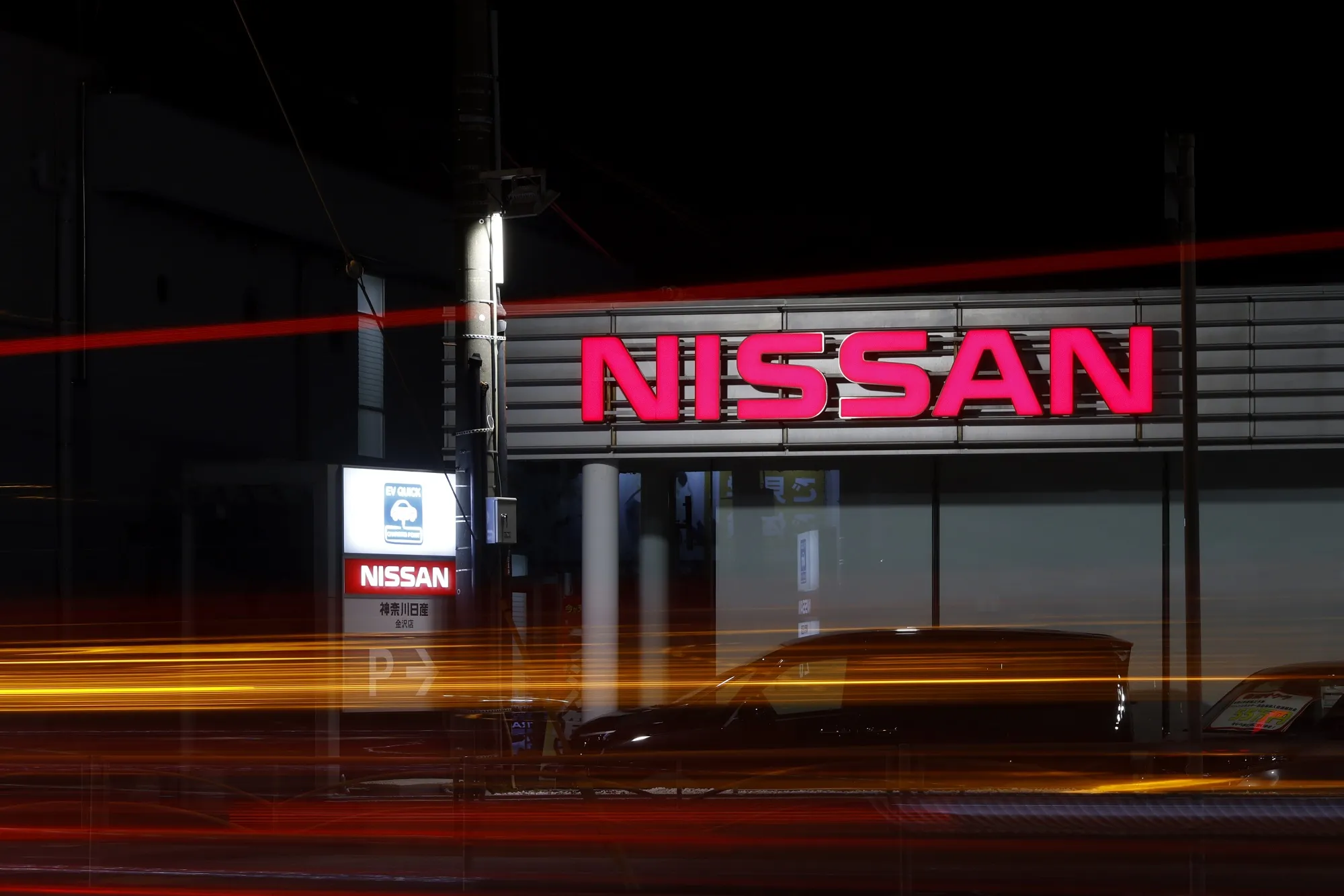 Vehicles leave light trials as they pass a Nissan Motors Co. dealership.