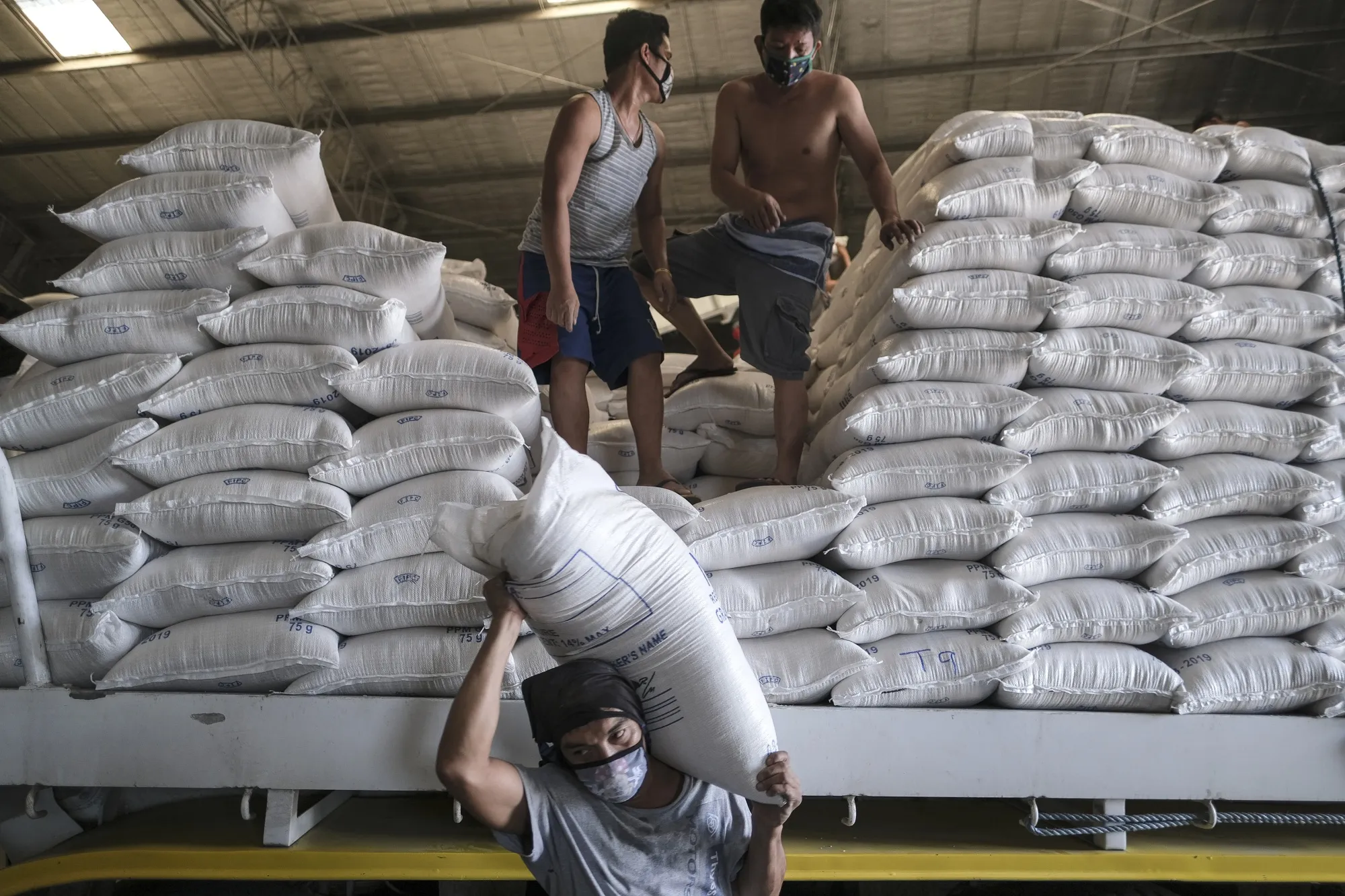 Workers wearing protective masks unload sacks of rice inside a National Food Authority warehouse in Valenzuela, Metro Manila, the Philippines, on March 26.&nbsp;