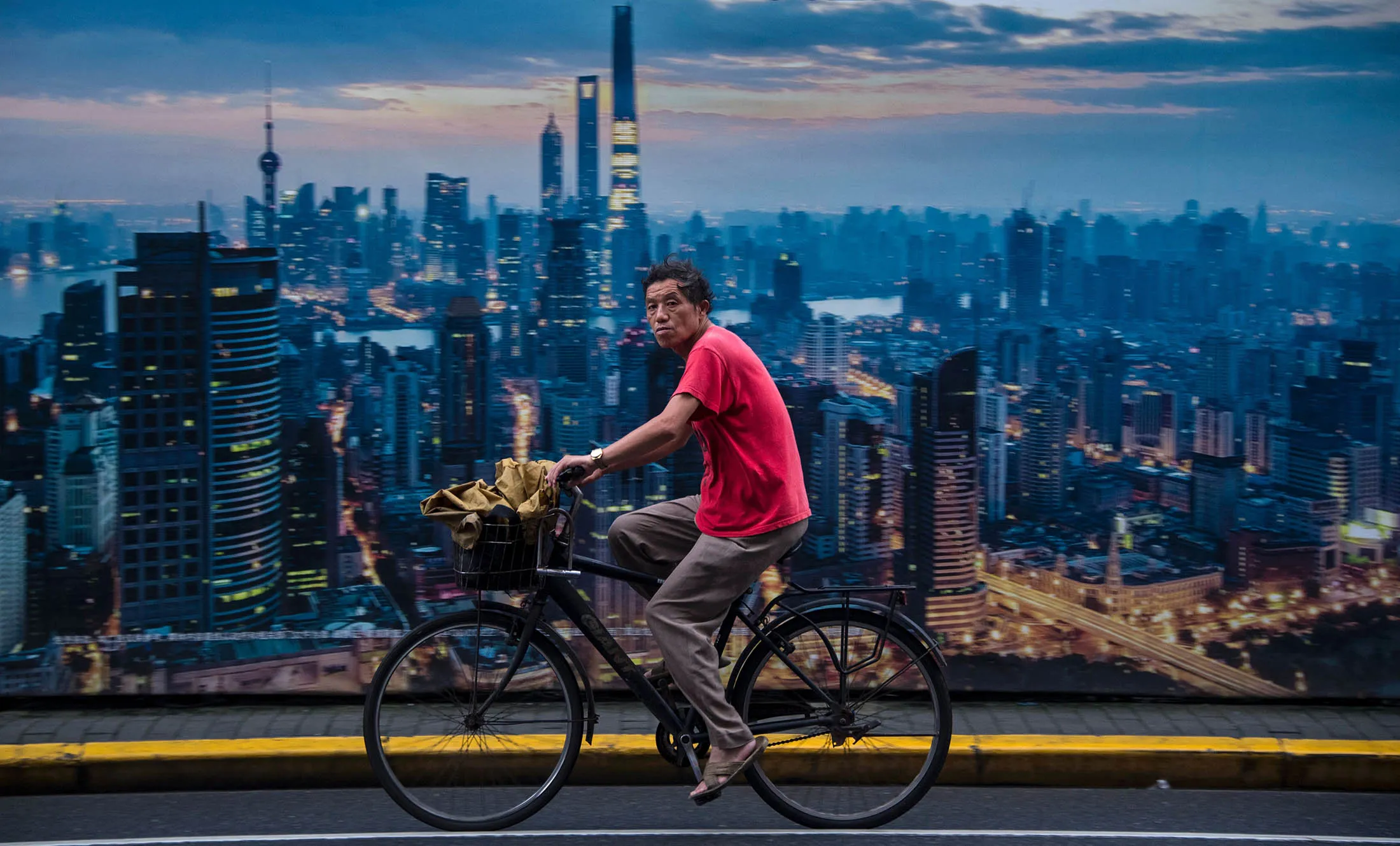 This picture taken on July 11, 2016 shows a man cycling past a billboard showing an aerial view of Shanghai. China's growth slipped to a new seven-year low of 6.6 percent in the second quarter, according to a survey of economists by AFP, despite government efforts to spur activity in the world's second-largest economy. / AFP / JOHANNES EISELE / TO GO WITH China-economy-growth-GDP,POLL by Bill Savadove (Photo credit should read JOHANNES EISELE/AFP/Getty Images)
