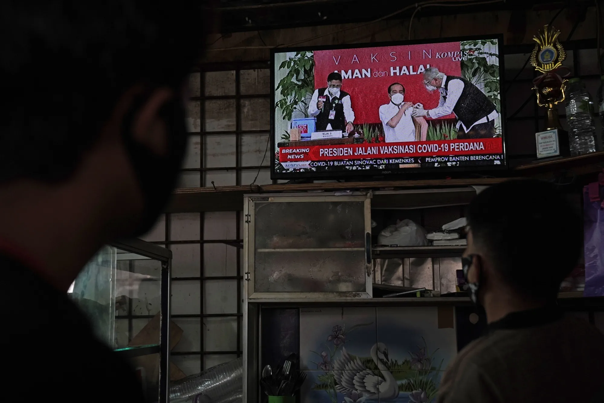 People watch a live news broadcast of Joko Widodo receiving a dose of Sinovac Biotech Covid-19 vaccine, in Jakarta, on Jan. 13.