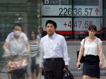 People walk past a stock indicator showing share prices on the Tokyo Stock Exchange.
