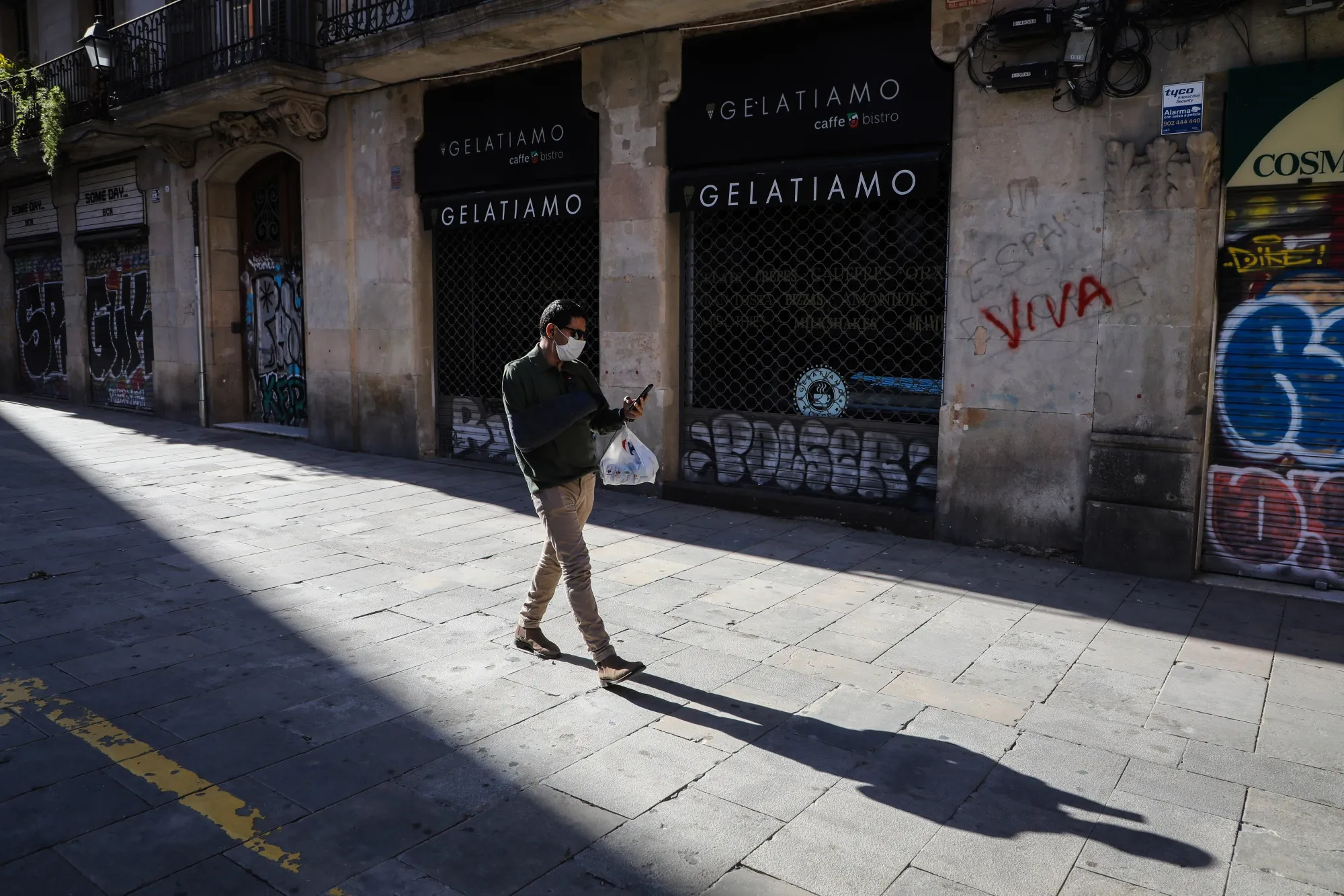 A pedestrian wearing a protective face mask walks past shuttered stores in Barcelona, on April 30.