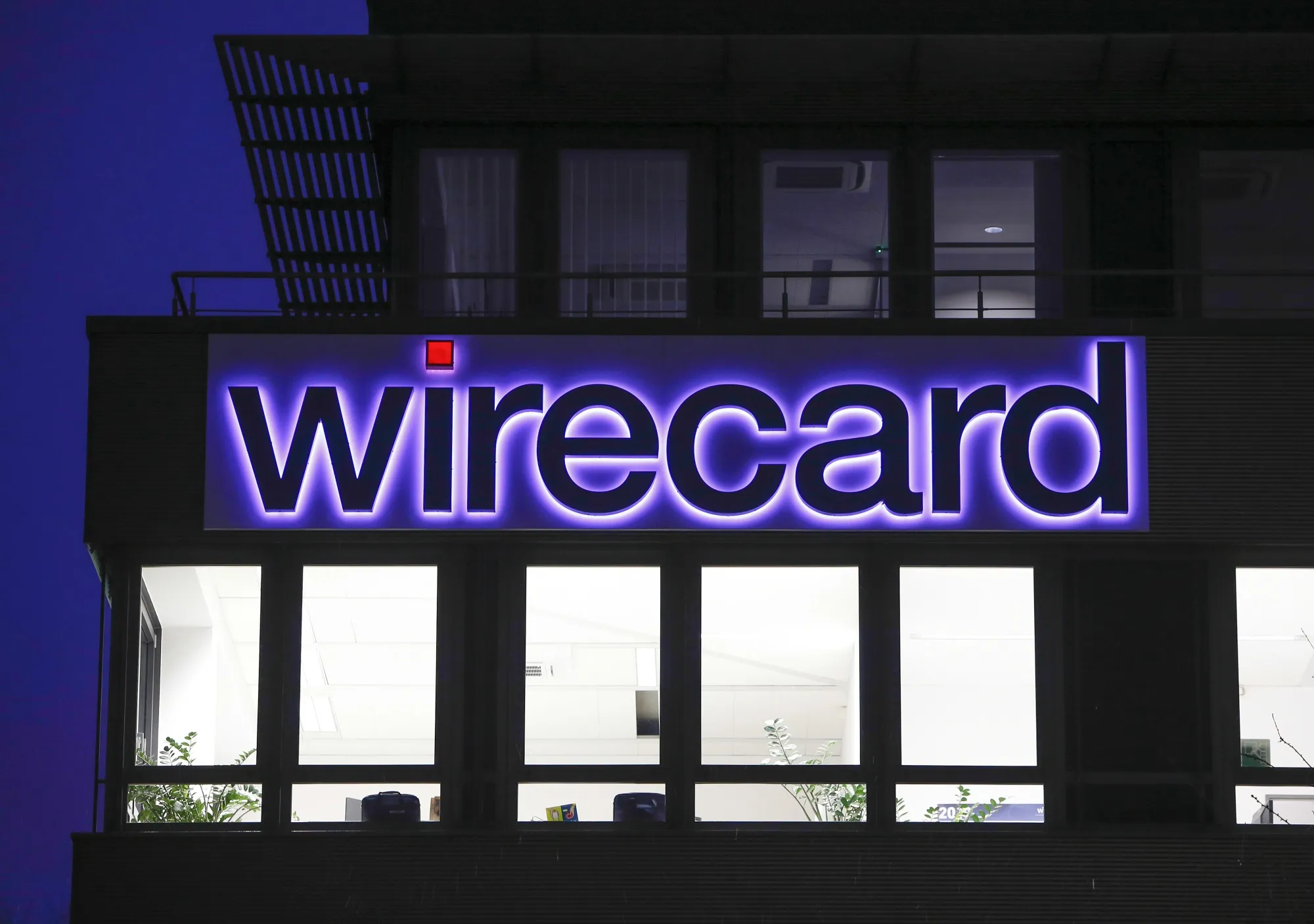 An logo sits above illuminated office windows at the Wirecard AG headquarters at dawn in the Aschheim district of Munich, Germany.