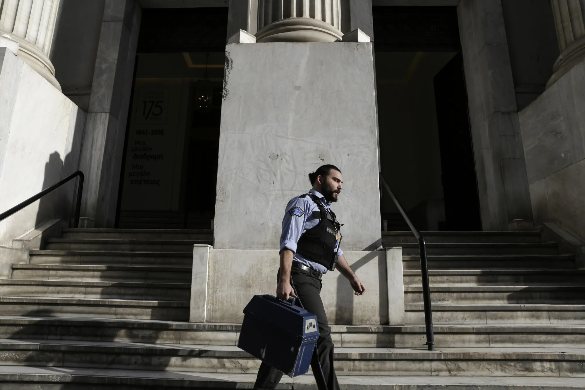 A security guard carries a cash box from the central branch of the National Bank of Greece SA in Thessaloniki.