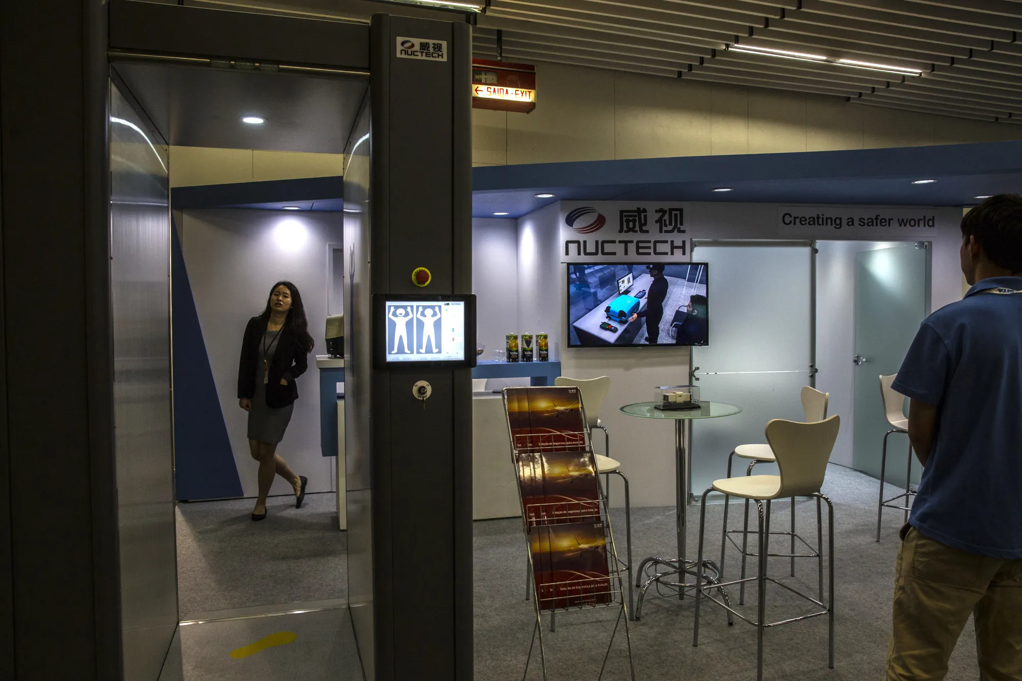 A person watches a television screen showing a baggage scan next to a Nuctech Co. personnel screening device in Rio de Janeiro.