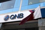 A Qatar national flag flies outside a branch of the Qatar National Bank SAQ (QNB) in Doha, Qatar.