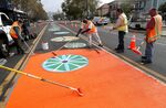 Workers apply orange coating along 90th Avenue in East Oakland, California, in 2019&nbsp;as part of a&nbsp;paving and redesign project for pedestrian and bicyclist safety.&nbsp;