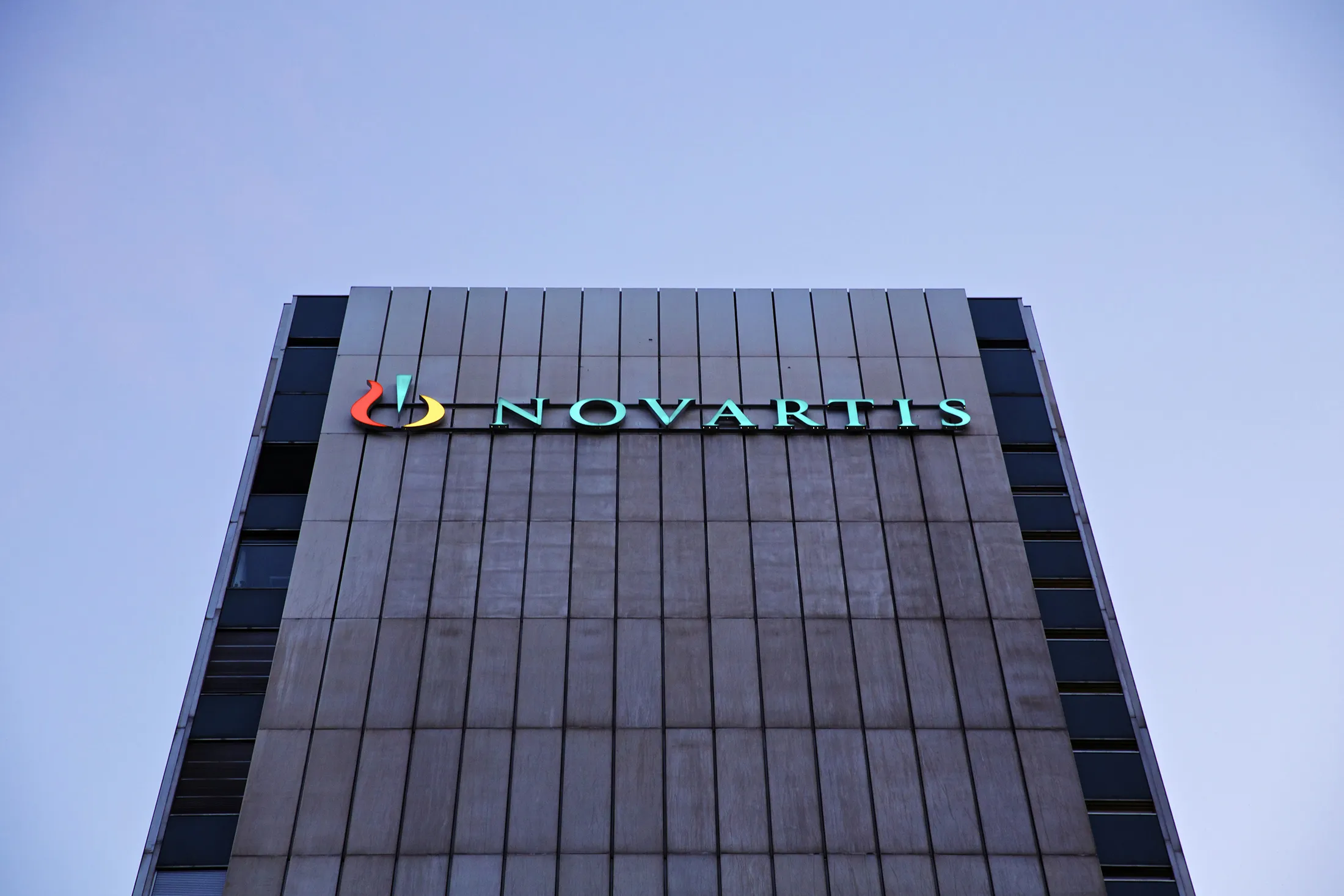 An illuminated logo sits outside Novartis AG's headquarters in Basel, Switzerland, on Tuesday, July, 16, 2013. Novartis AG raised its profit and sales forecasts as generic competition for the Diovan blood-pressure medicine failed to materialize in the U.S.