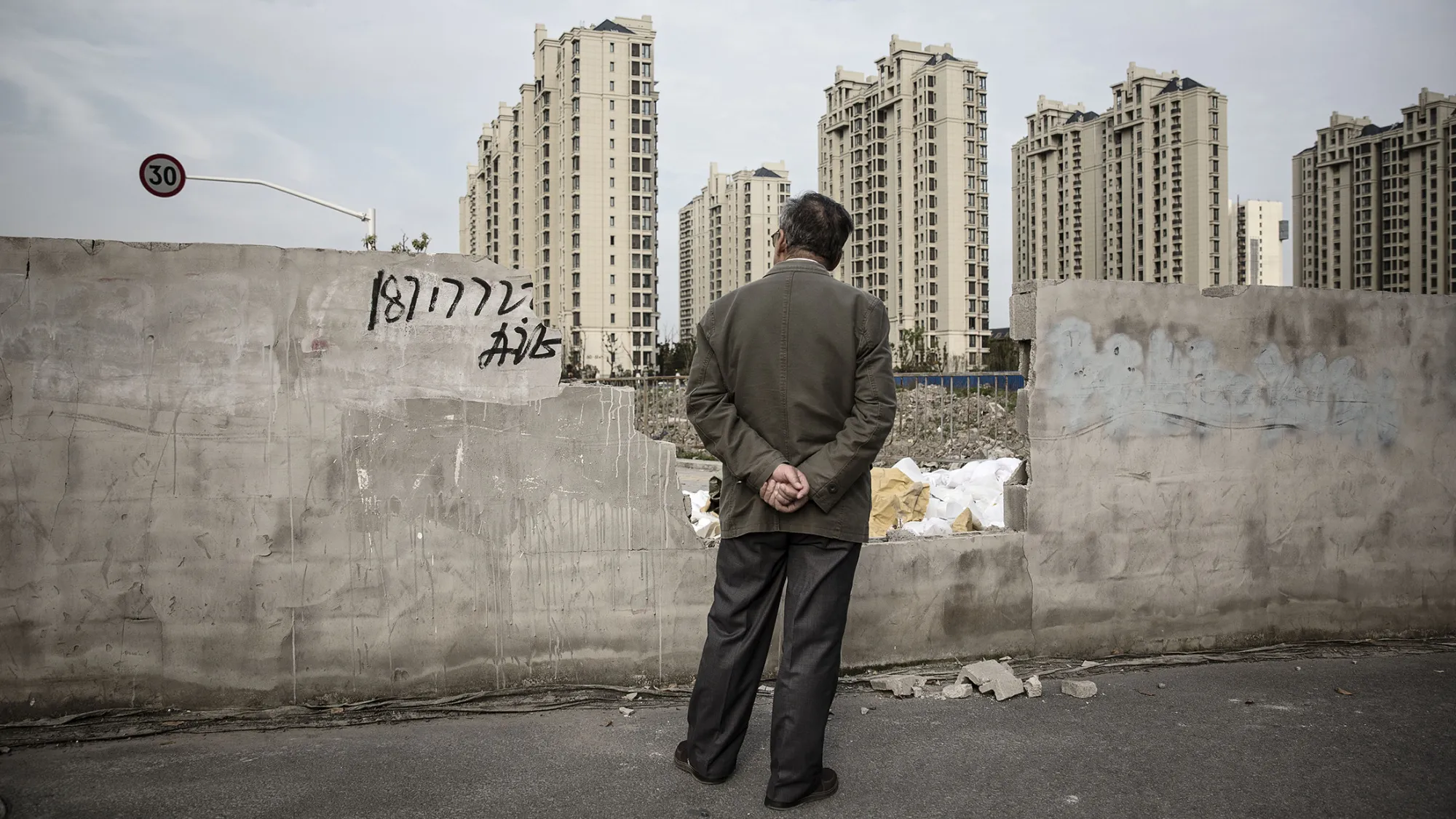A man looks out from an opening in a wall as residential buildings stand in the distance in the Jiading district of Shanghai, China, on Monday, April 11, 2016. China's economy stabilized last quarter and gathered pace in March as a surge in new credit helped the property sector rebound while raising fresh question marks over the sustainability of the debt-fueled expansion.
