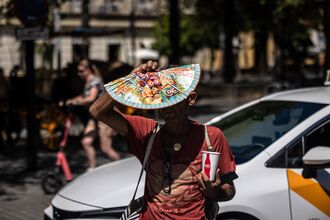 A pedestrian uses a fan for shade in Seville