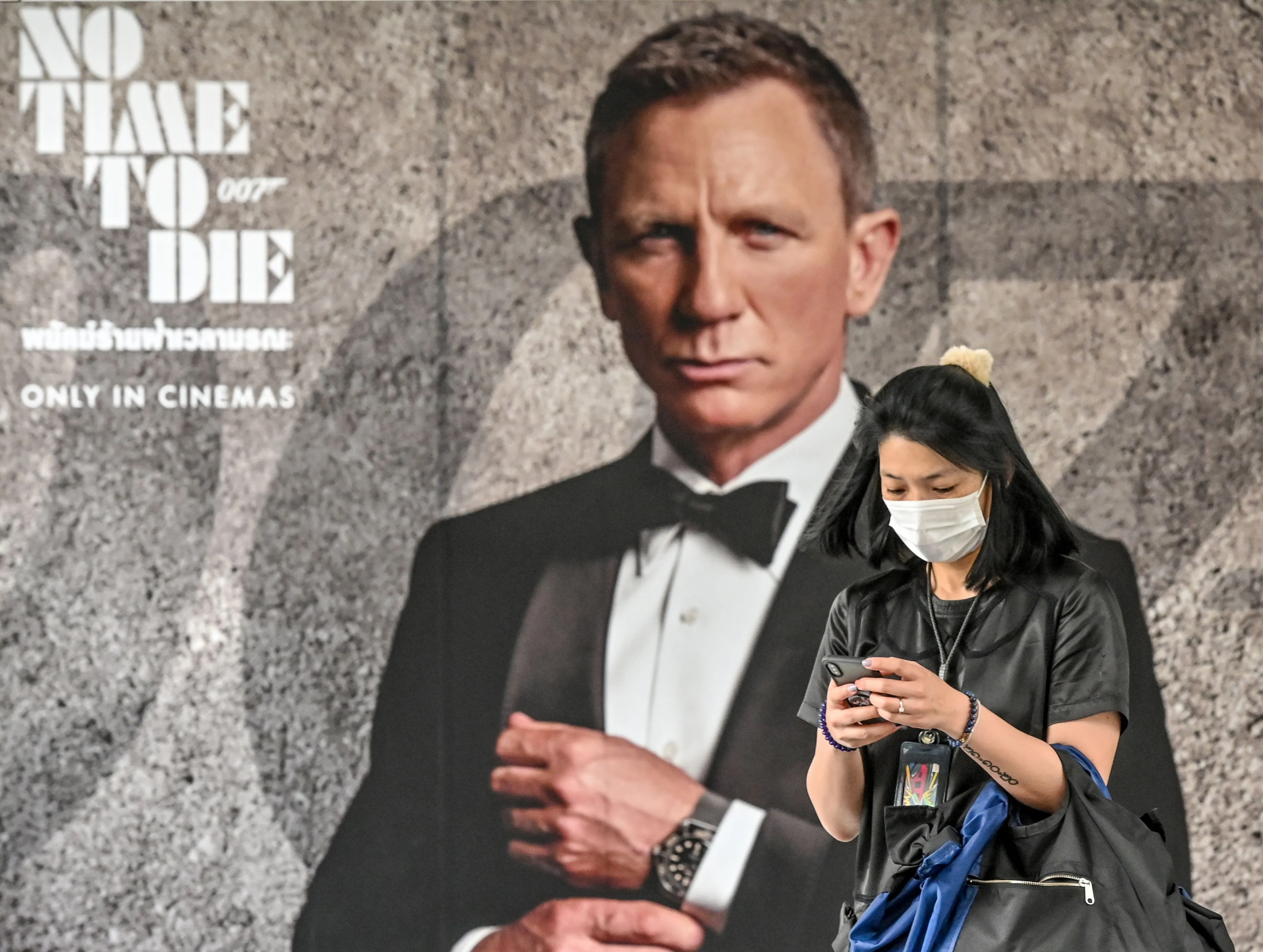 A woman wearing a facemask amid fears of the spread of the COVID-19 novel coronavirus walks past a poster for the new James Bond movie "No Time to Die" in Bangkok on February 28, 2020.