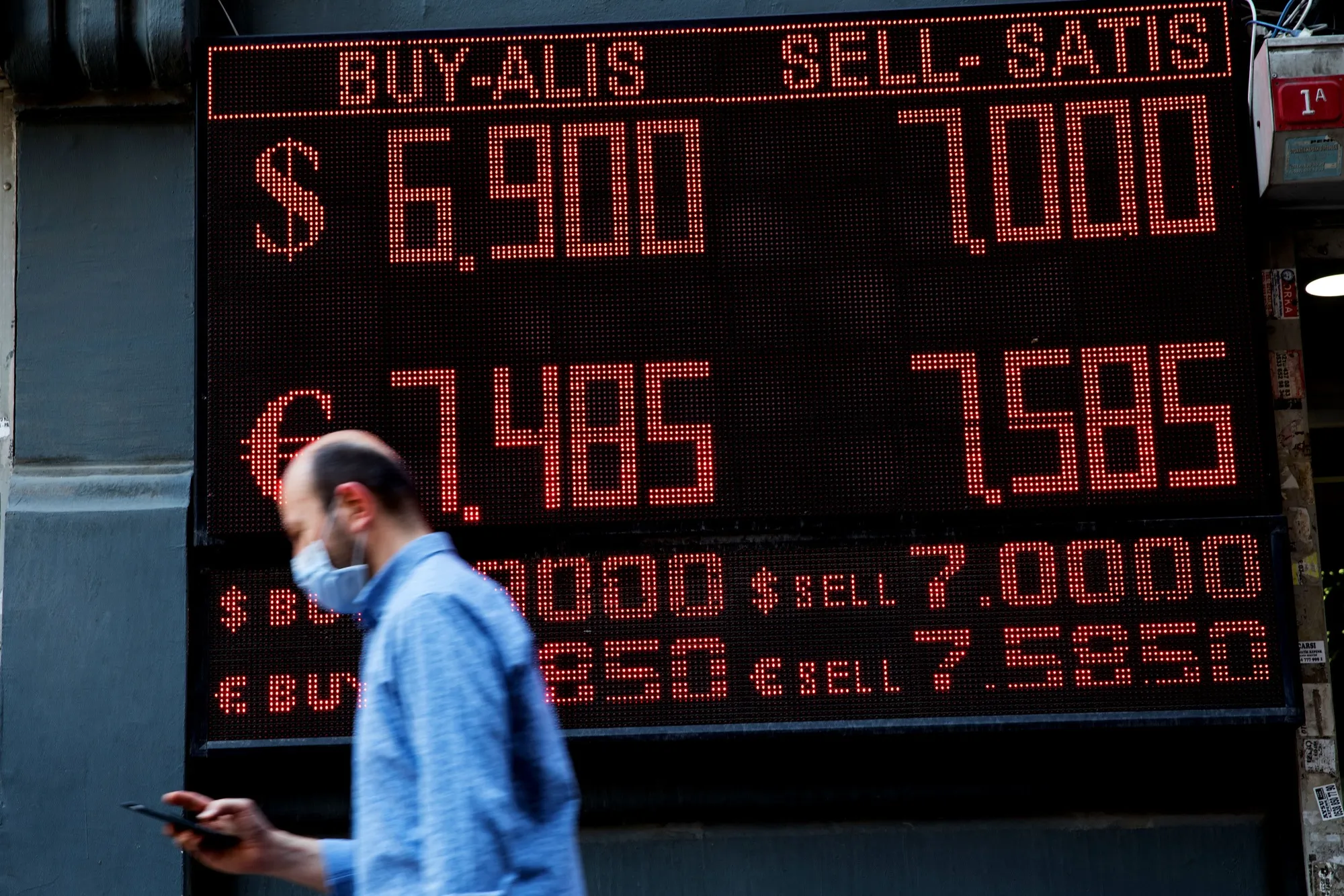 A pedestrian wearing a protective face mask checks his smartphone while passing an electronic currency exchange rate board in Istanbul, Turkey, on&nbsp;April 27.