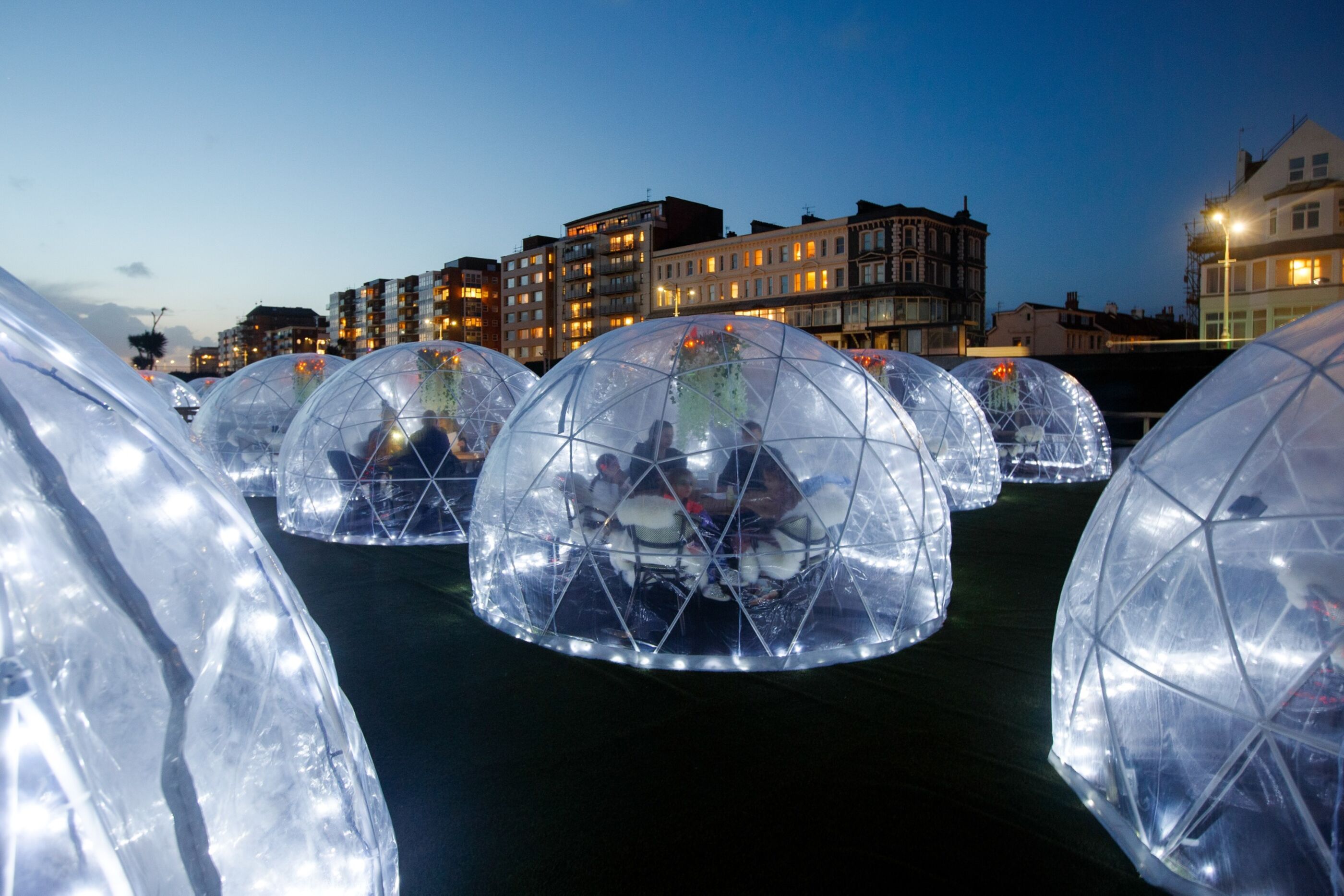 Rows of plastic domes outside, with diners seated inside each one at a table to eat.