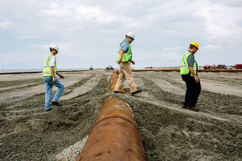 Members of the Louisiana Coastal Protection and Restoration Authority walk over pipeline on the beach at Port Fourchon, site of the Caminada Headland Beach and Dune Restoration project.