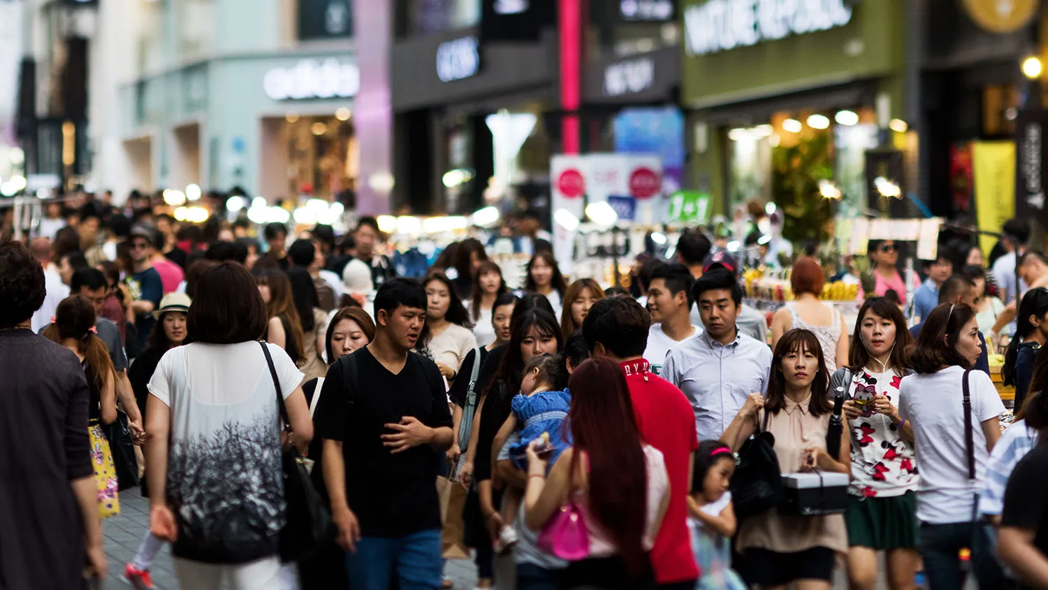 Shoppers and pedestrians walk past stores in the Myeongdong shopping district in this photograph taken with a tilt-shift lens in Seoul, South Korea, on July 18, 2015.
