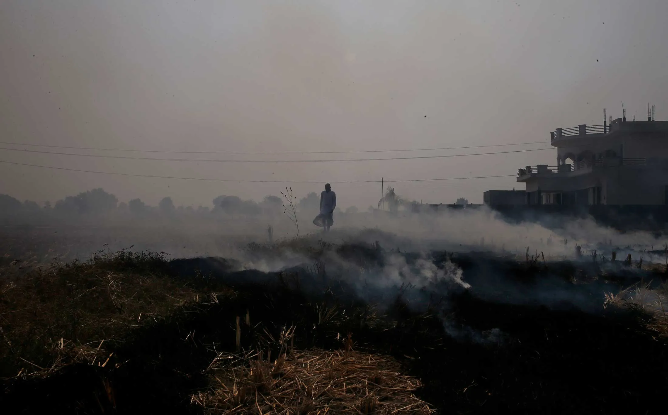 A&nbsp;farmer walks through smoke from the fire he set to clear a field at Chandhat, India.