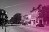 Main street of Fond du Lac, the picture is in black and white with a pink gradient on top. The street is empty, with a couple of cars parked on the side of the road. American flags are hanging off streetlights.