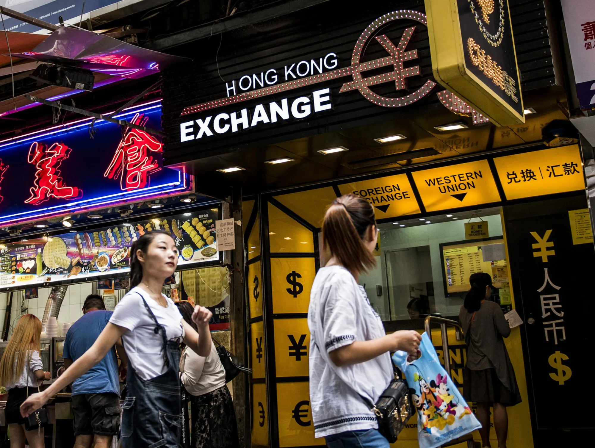 Pedestrians walk past a currency exchange store in Hong Kong.
