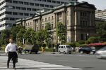 A pedestrian crosses a road while traffic drives past the Bank of Japan headquarters in Tokyo, Japan.
