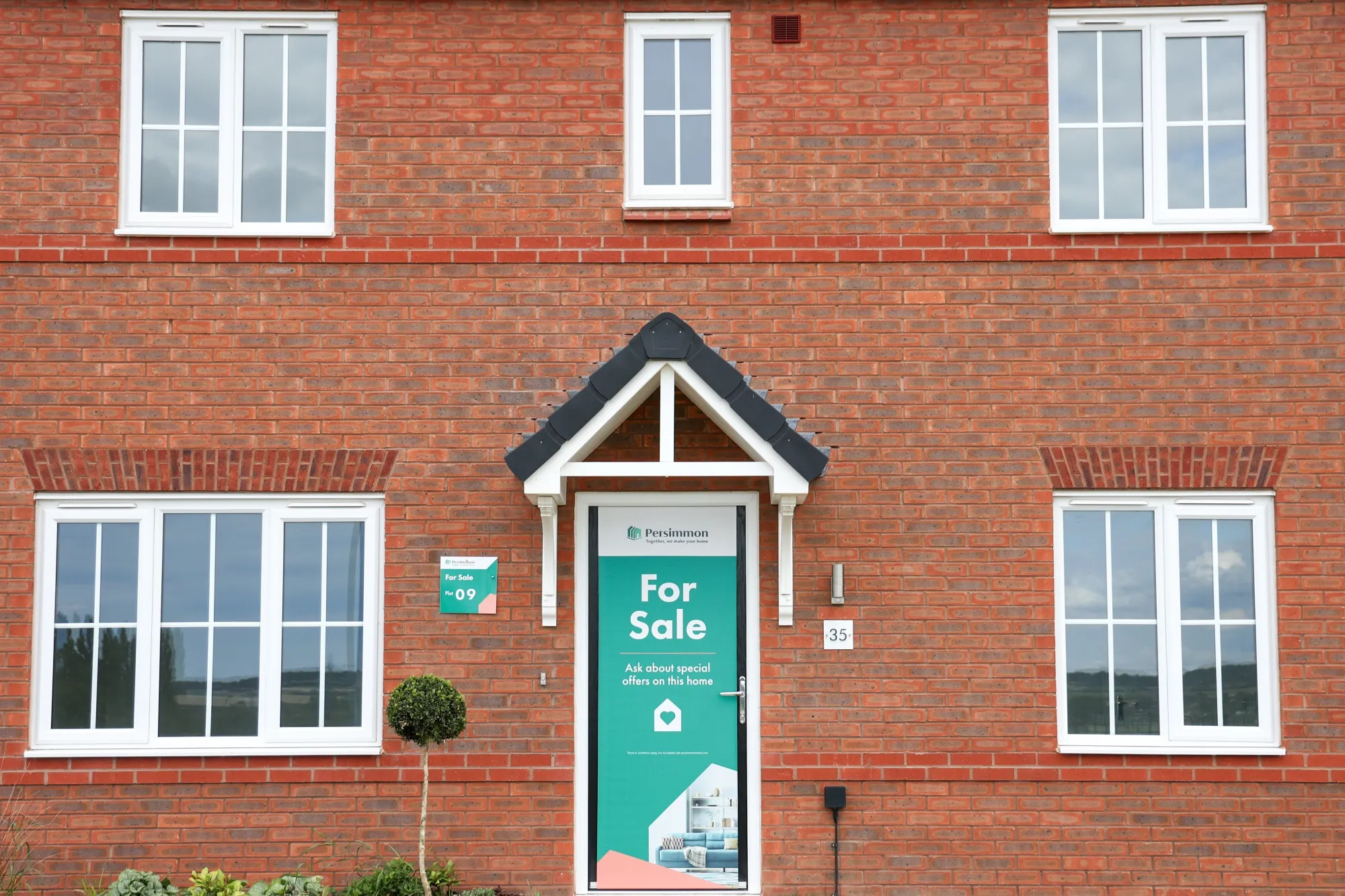 A "For Sale" sign on the front door of a recently completed house.