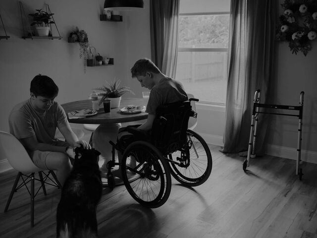 Michael Brewer and his brother Brady sit at a table with their dog nearby.