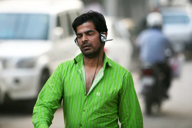 A man with headphones on his ears walks along a road in New Delhi