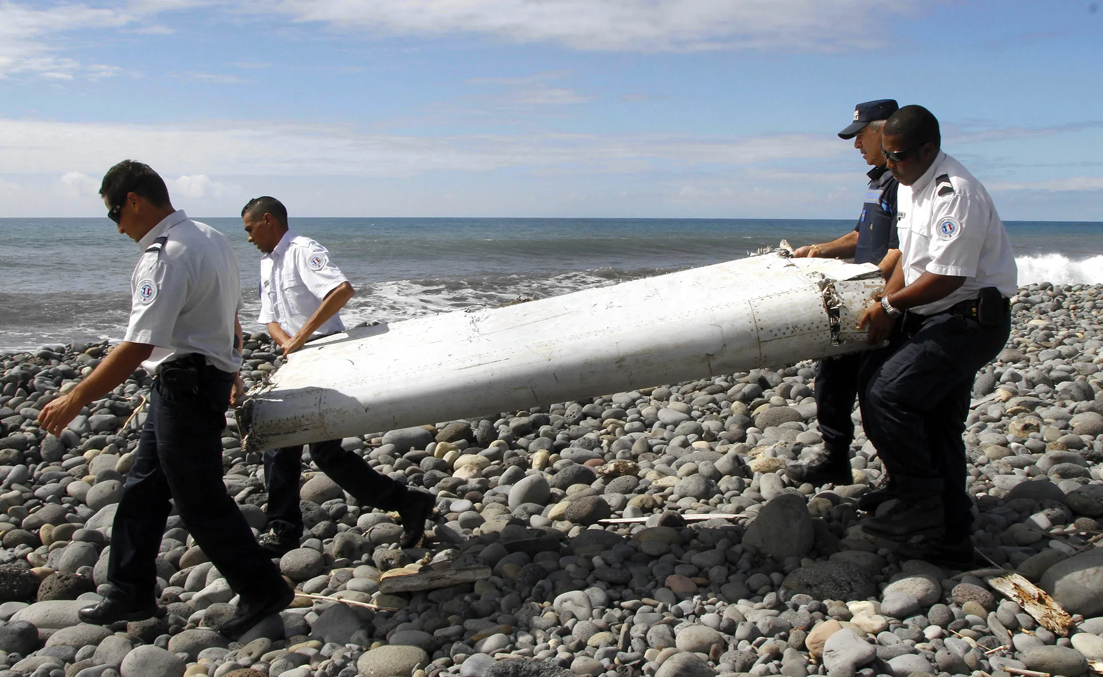 Police officers carry a piece of debris from the plane, that washed up on a beach in Saint-Andre de la Reunion, on July 29, 2015.
