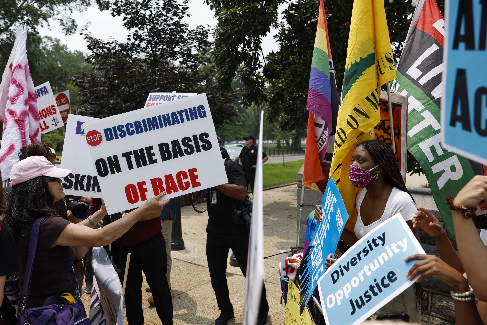 Photograph of protestors holding signs saying "stop discriminating on the basis of race" and "diversity, opportunity, justice".