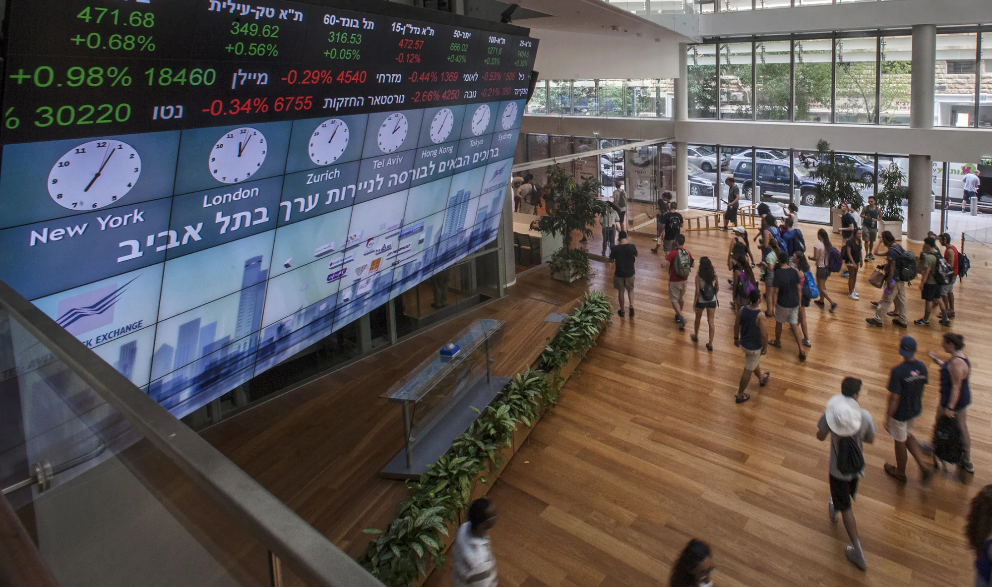 Visitors stand in front of a stock market ticker screen in the lobby of the Tel Aviv Stock Exchange.
