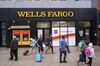 Front of Wells Fargo branch with ATM soon opening with pedestrians walking past with carry-on luggage, in July 2019