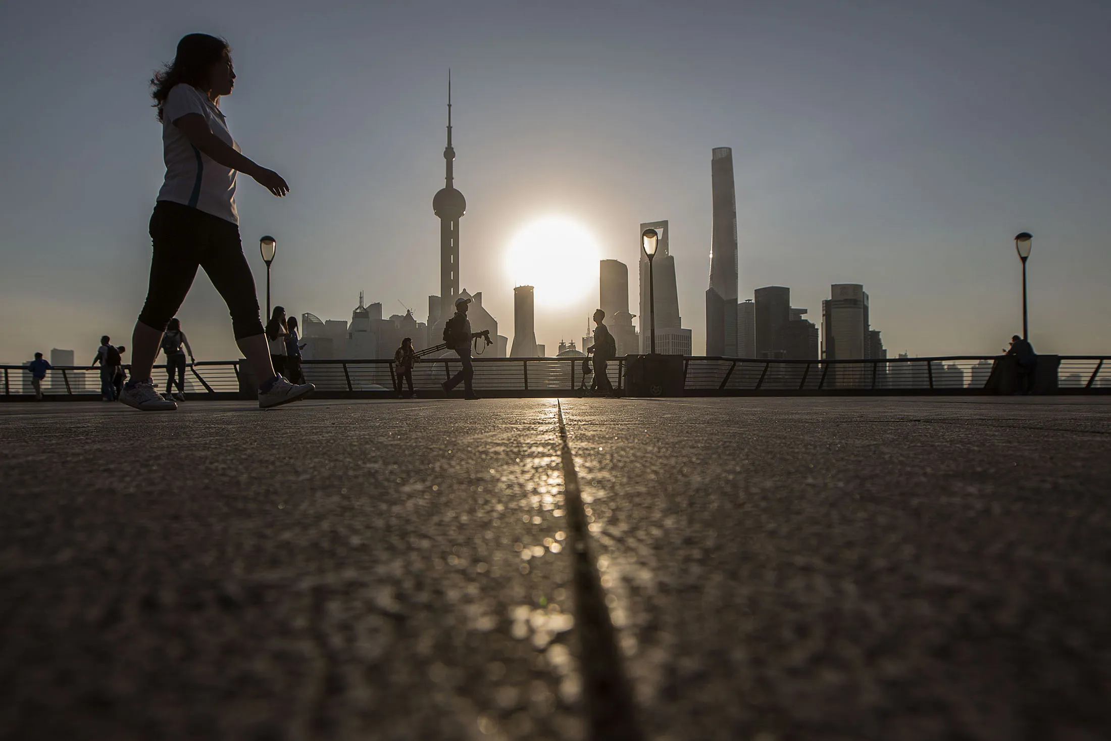 People out for morning exercises walk down the Bund with the buildings of Pudong's Lujiazui Financial District silhouetted in the background in Shanghai, China, on Friday, Oct. 02, 2015.

