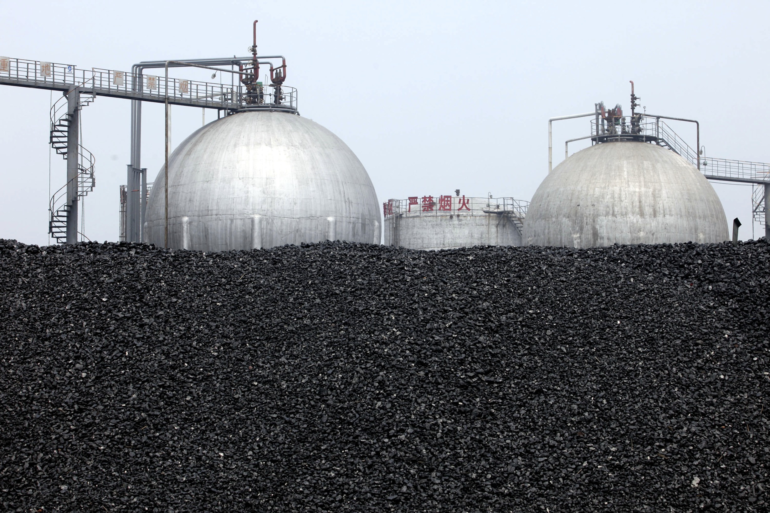 Coal is piled near methanol tanks at the China XLX Fertiliser Ltd. plant in Xinxiang, Henan province, China, on Saturday, May 29, 2010. China XLX Fertiliser Ltd. manufactures urea and compound fertilizer from coal. The company also produces methanol.