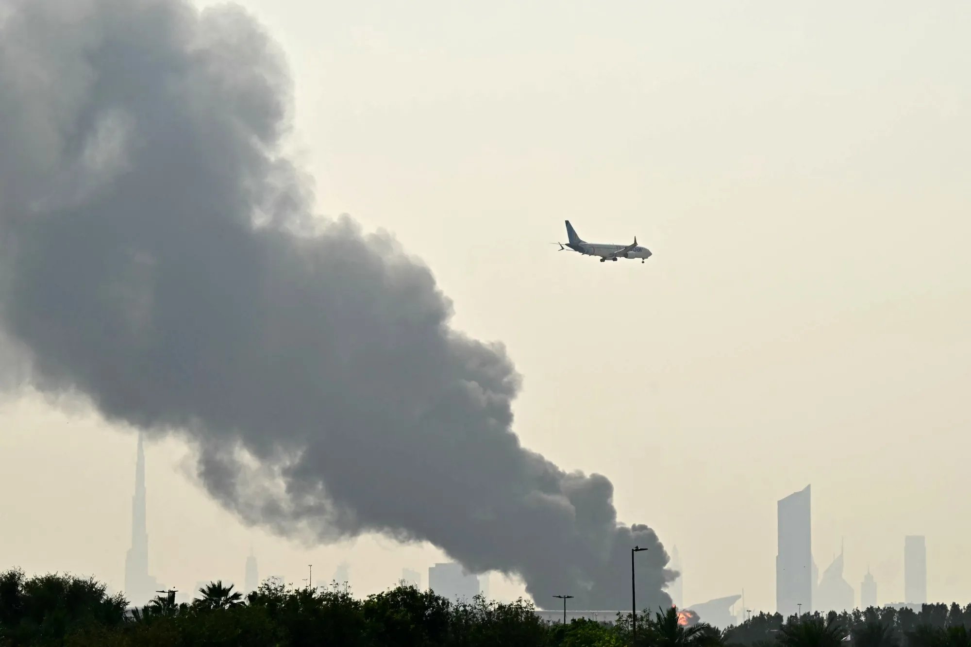 An Emirates aircraft flies past plumes of smoke from a&nbsp;fire near Dubai International Airport on March 16.