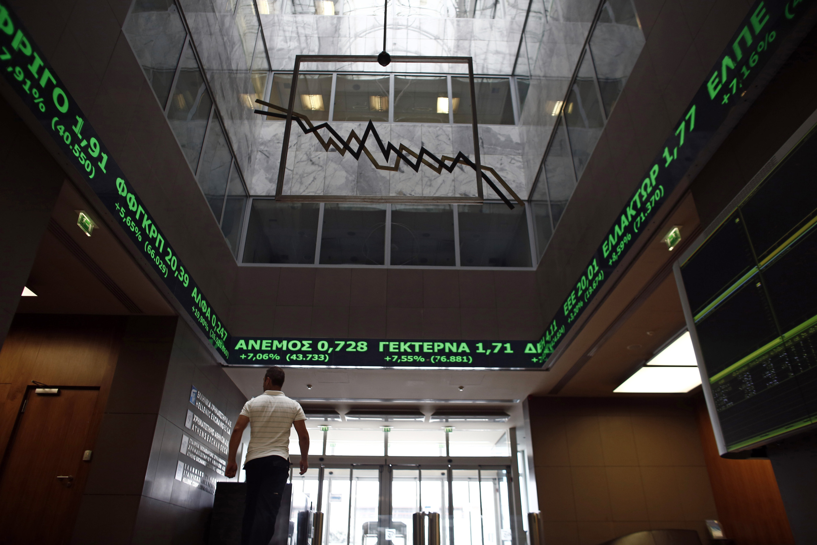A visitor passes beneath a stock price ticker screen inside the Hellenic stock exchange in Athens.