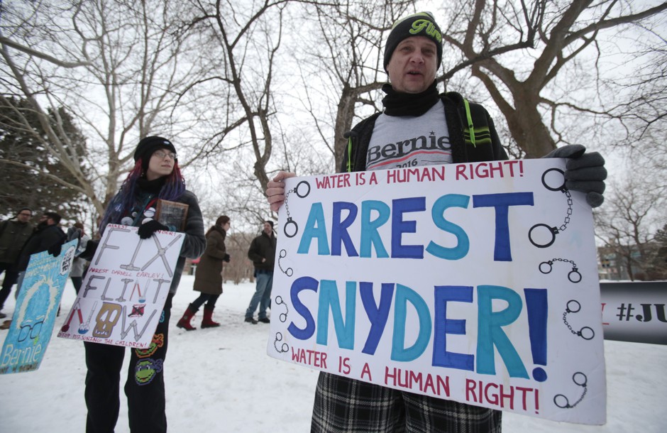 Demonstrators protesting in Flint, Michigan, over the contaminated water crisis with signs referencing Michigan Governor Rick Snyder, March 6, 2016.
