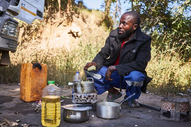 A truck driver prepares a roadside meal while waiting in a days-long queue to cross the Congo-Zambia border. 